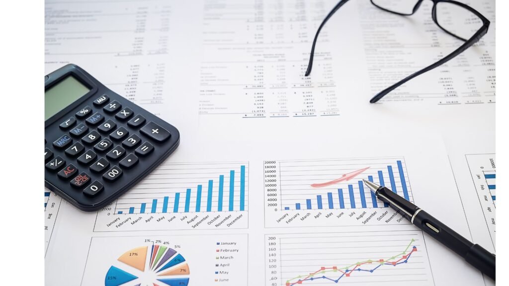 Financial charts, a calculator, pen, and glasses on a desk