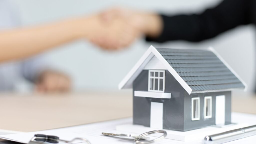 Model house, keys on table, and handshake in background.